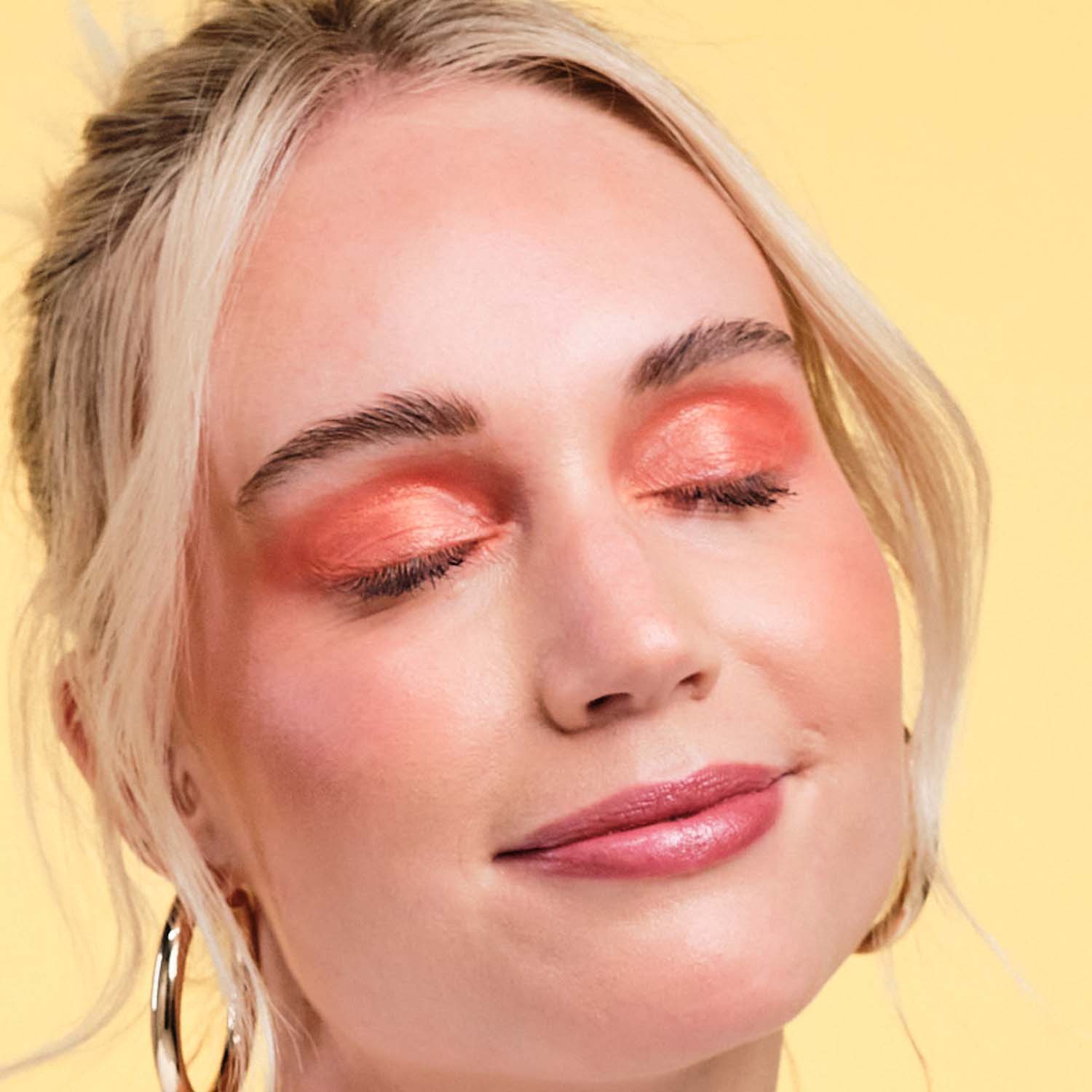 Model with closed eyes wearing orange eyeshadow